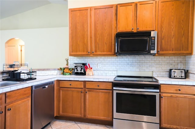 kitchen with tile countertops, tasteful backsplash, appliances with stainless steel finishes, and light tile patterned flooring