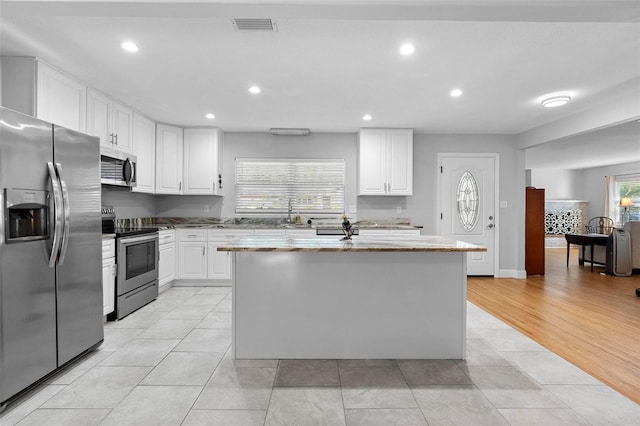 kitchen featuring light stone countertops, a kitchen island, white cabinetry, and stainless steel appliances