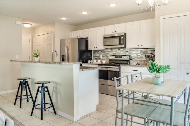 kitchen with light tile patterned floors, backsplash, appliances with stainless steel finishes, white cabinetry, and a kitchen breakfast bar