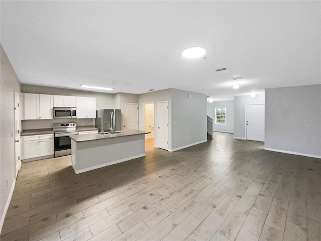 kitchen featuring light wood-style flooring, white cabinetry, open floor plan, appliances with stainless steel finishes, and a center island with sink