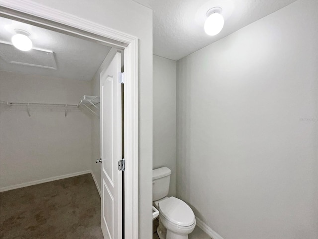 bathroom with a walk in closet, baseboards, and toilet