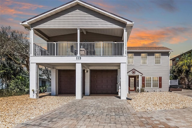 raised beach house with decorative driveway, a balcony, and an attached garage