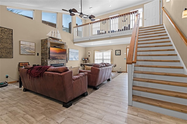 living area featuring baseboards, a ceiling fan, stairway, wood finish floors, and a fireplace