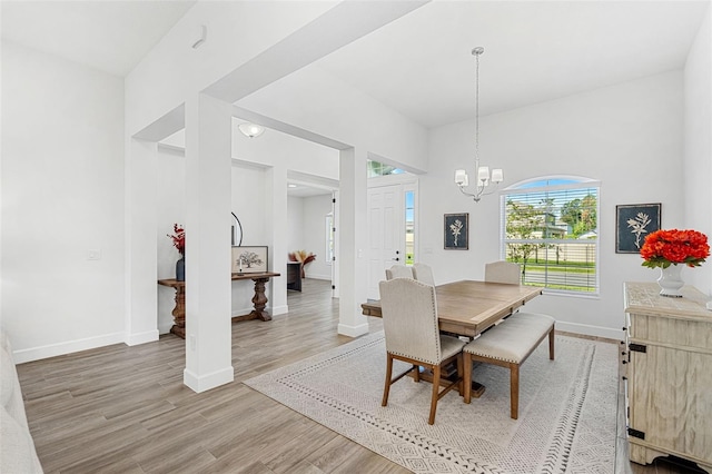 dining room with light wood-type flooring, a towering ceiling, baseboards, and a notable chandelier