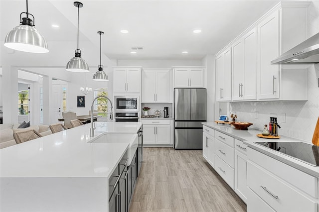 kitchen featuring wall chimney exhaust hood, a healthy amount of sunlight, stainless steel appliances, and light countertops