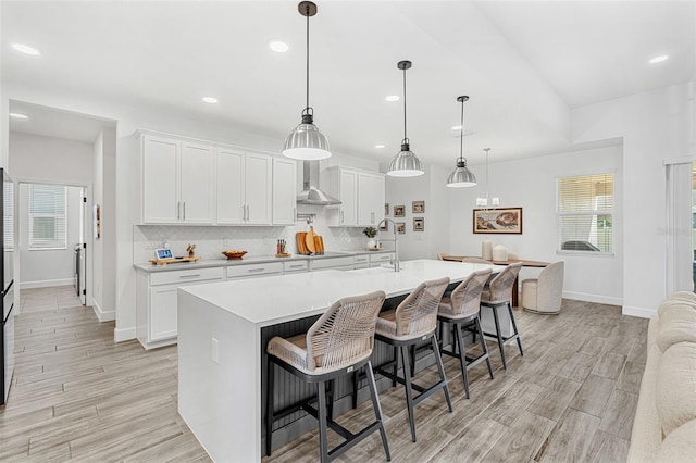 kitchen with baseboards, wall chimney exhaust hood, a sink, and light countertops