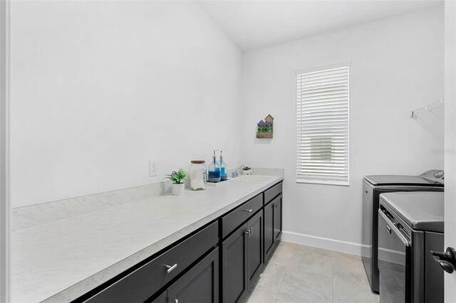 laundry area featuring washer and clothes dryer, a sink, light tile patterned flooring, baseboards, and cabinet space