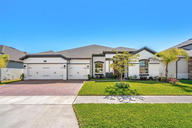 view of front of home with stucco siding, an attached garage, decorative driveway, and a front yard