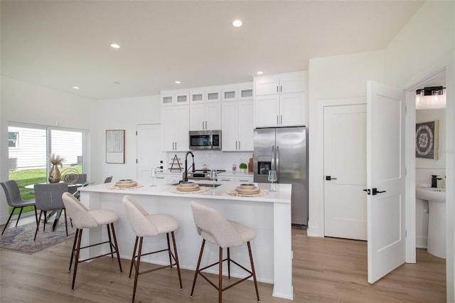 kitchen with an island with sink, light wood-style floors, stainless steel appliances, and a kitchen breakfast bar