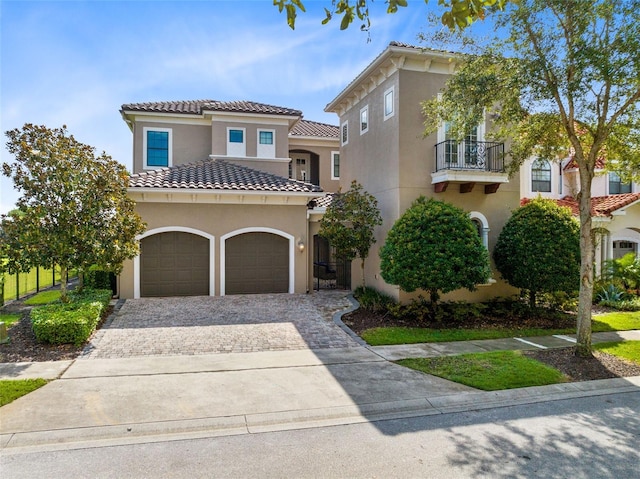 mediterranean / spanish house with decorative driveway, a tile roof, a balcony, and stucco siding