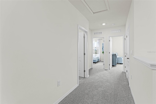 corridor with baseboards, attic access, visible vents, and light colored carpet