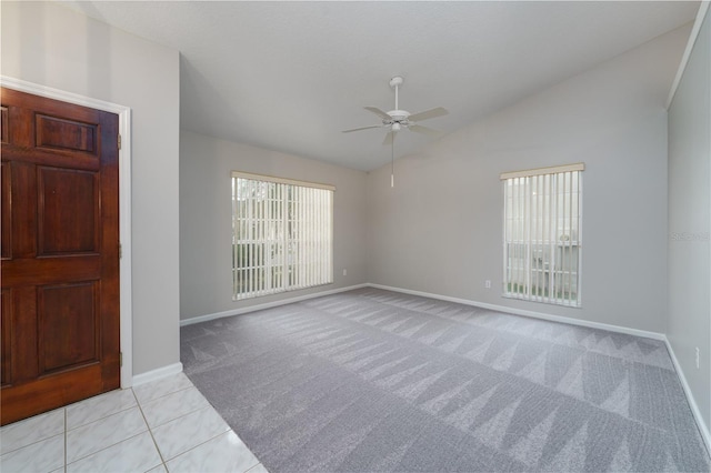 spare room with ceiling fan, light tile patterned floors, light colored carpet, baseboards, and vaulted ceiling