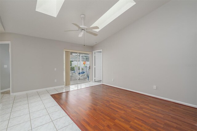 empty room featuring ceiling fan, light wood-style floors, lofted ceiling with skylight, and baseboards