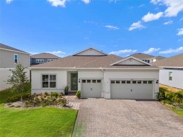 ranch-style home with a garage, roof with shingles, decorative driveway, a front yard, and stucco siding