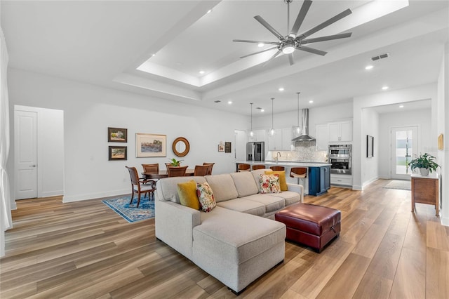 living area with light wood-type flooring, a raised ceiling, visible vents, and baseboards