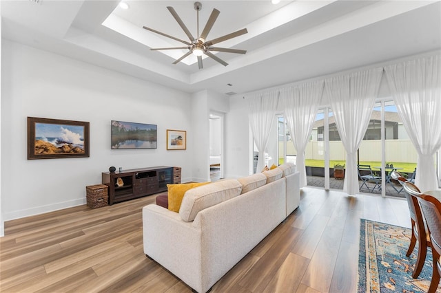 living area with a healthy amount of sunlight, baseboards, a raised ceiling, and wood finished floors