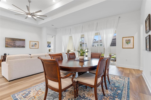 dining room with light wood-type flooring, a raised ceiling, ceiling fan, and baseboards