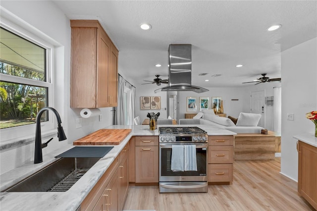 kitchen with open floor plan, a peninsula, stainless steel gas range, island exhaust hood, and a sink