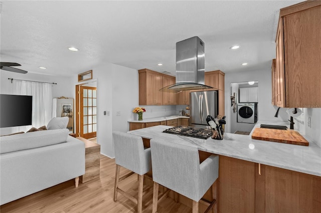 kitchen with island exhaust hood, gas stovetop, washer / clothes dryer, freestanding refrigerator, and a peninsula