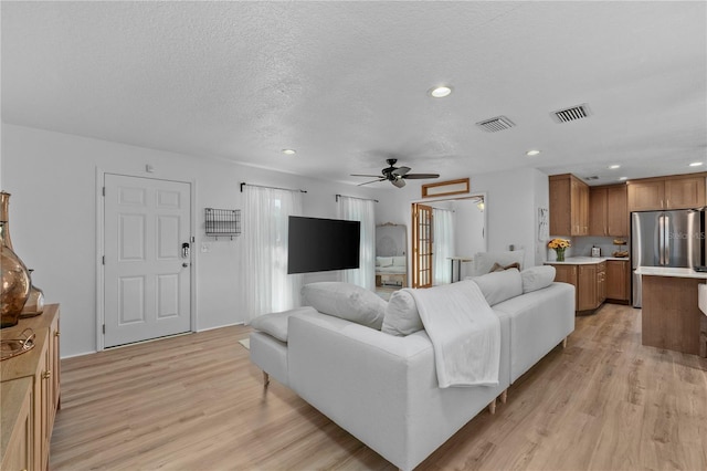 living room featuring a textured ceiling, light wood-type flooring, visible vents, and recessed lighting