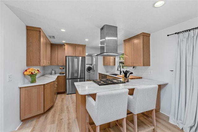 kitchen featuring a sink, gas cooktop, island range hood, stainless steel fridge, and a peninsula