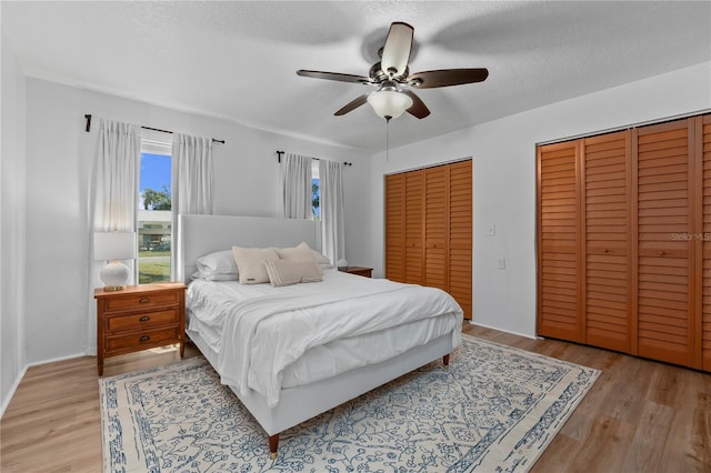 bedroom with a textured ceiling, a ceiling fan, two closets, and wood finished floors