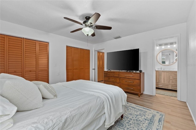 bedroom featuring two closets, visible vents, ensuite bathroom, light wood-style floors, and ceiling fan