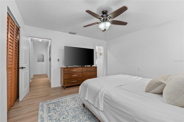 bedroom with light wood-type flooring, visible vents, ceiling fan, and a textured ceiling