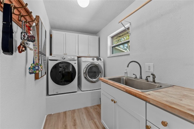 laundry room featuring a textured ceiling, a sink, light wood-style floors, cabinet space, and washing machine and clothes dryer