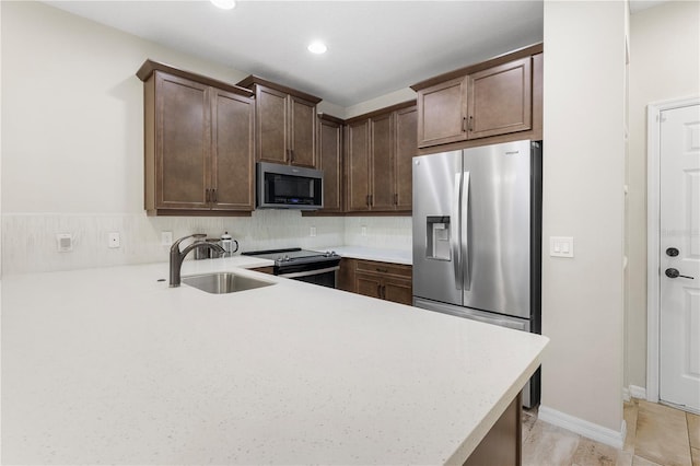 kitchen with dark brown cabinetry, a peninsula, stainless steel appliances, light countertops, and a sink