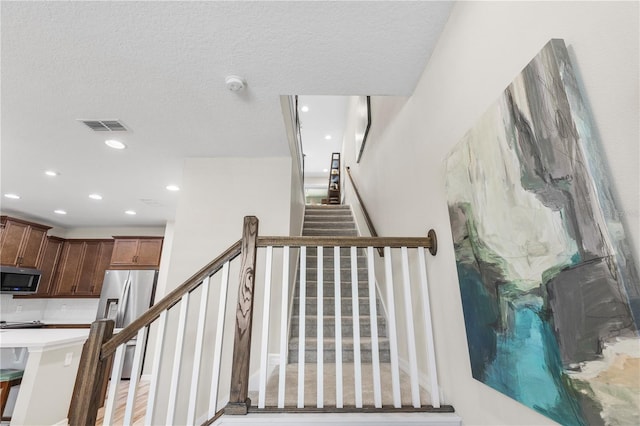 stairs featuring recessed lighting, visible vents, and a textured ceiling