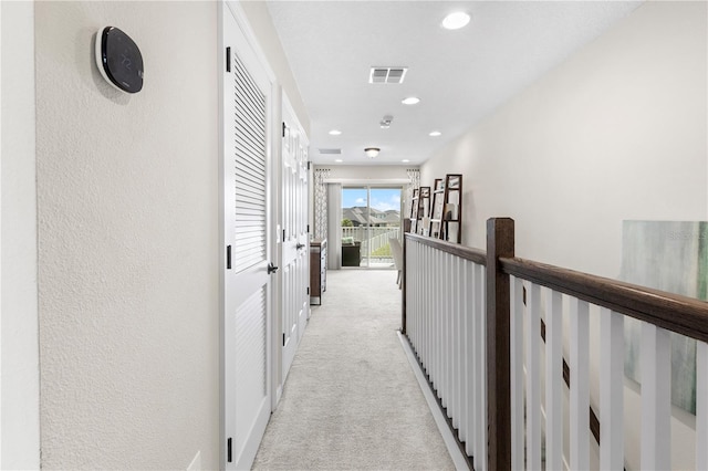 hallway with a textured wall, recessed lighting, visible vents, and light colored carpet