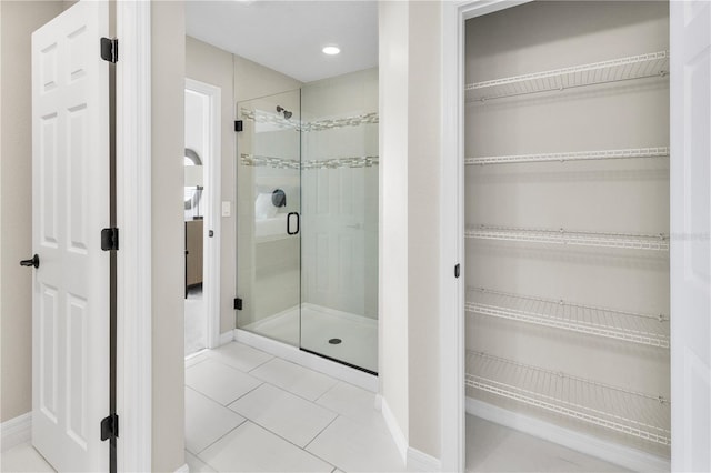 bathroom featuring a shower stall, baseboards, a walk in closet, and tile patterned floors