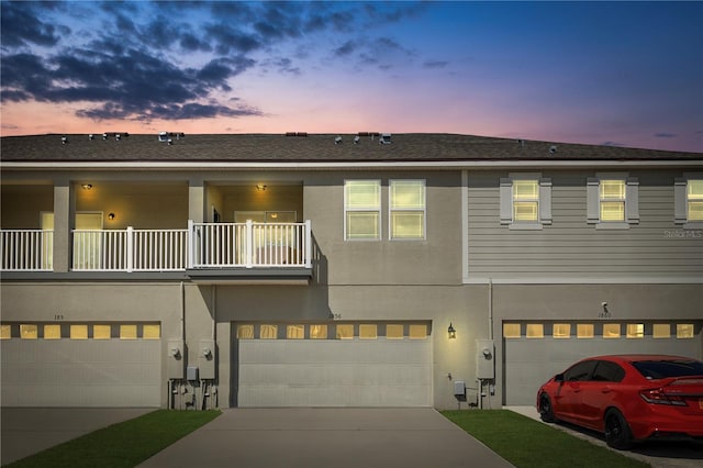 view of property featuring a balcony, a garage, concrete driveway, and stucco siding