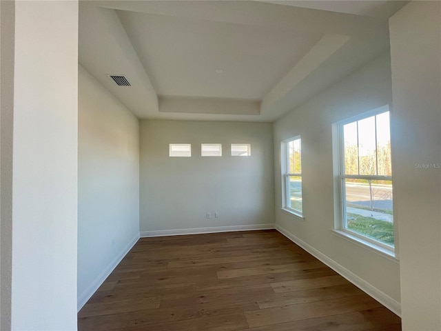 spare room featuring a tray ceiling, visible vents, baseboards, and wood finished floors