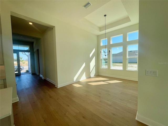 unfurnished room featuring a tray ceiling, hardwood / wood-style flooring, visible vents, and baseboards