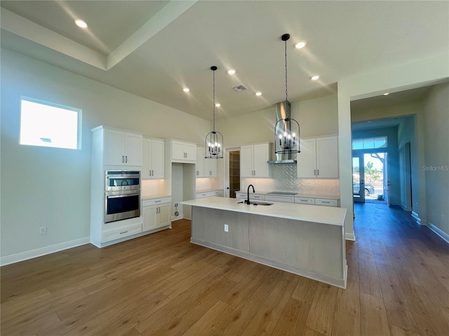 kitchen featuring wood finished floors, a sink, light countertops, white cabinetry, and backsplash