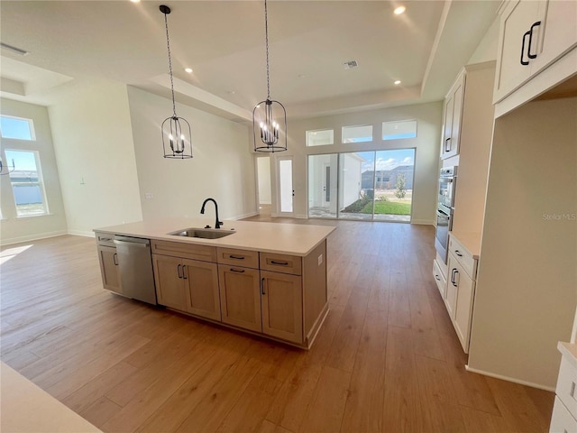 kitchen featuring a tray ceiling, appliances with stainless steel finishes, open floor plan, a sink, and light wood-type flooring