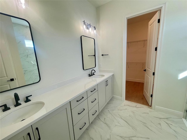 full bathroom with double vanity, marble finish floor, a spacious closet, and a sink