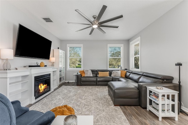 living room featuring baseboards, visible vents, a glass covered fireplace, ceiling fan, and wood finished floors