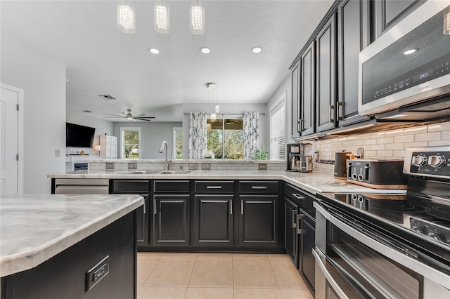 kitchen with light tile patterned flooring, dark cabinets, a sink, light countertops, and appliances with stainless steel finishes