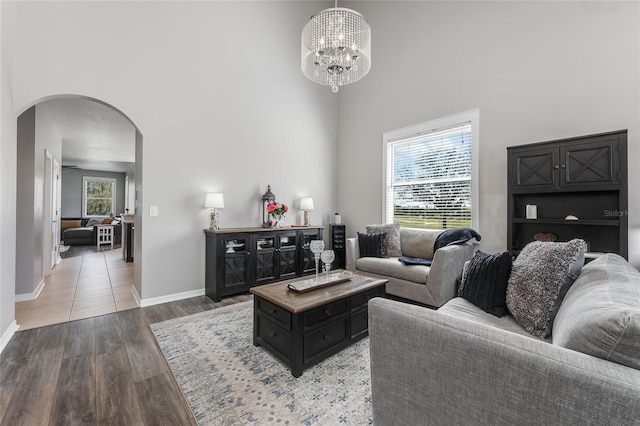 living area featuring arched walkways, a chandelier, a high ceiling, baseboards, and light wood-type flooring