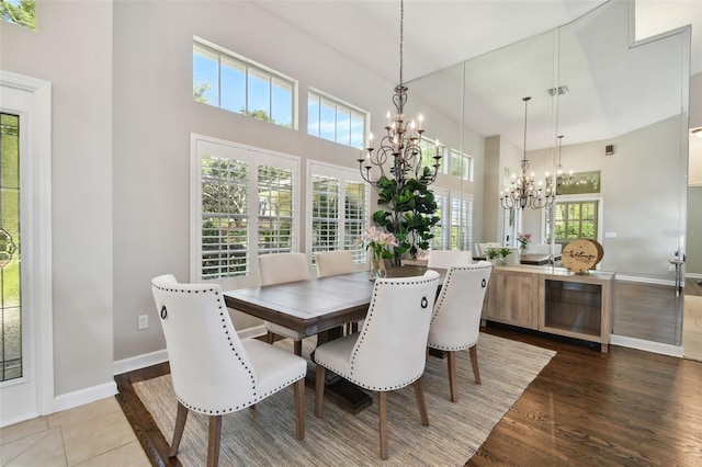 dining area with baseboards, visible vents, a towering ceiling, wood finished floors, and a chandelier