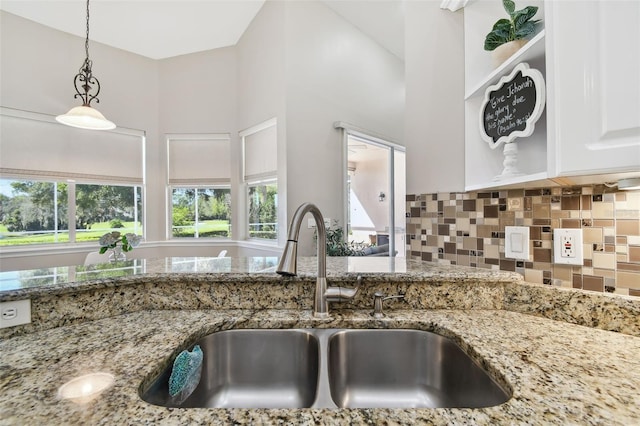 kitchen with tasteful backsplash, hanging light fixtures, light stone countertops, white cabinetry, and a sink