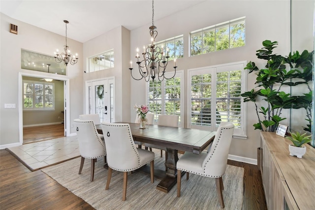 dining area with a towering ceiling, baseboards, dark wood finished floors, and a notable chandelier