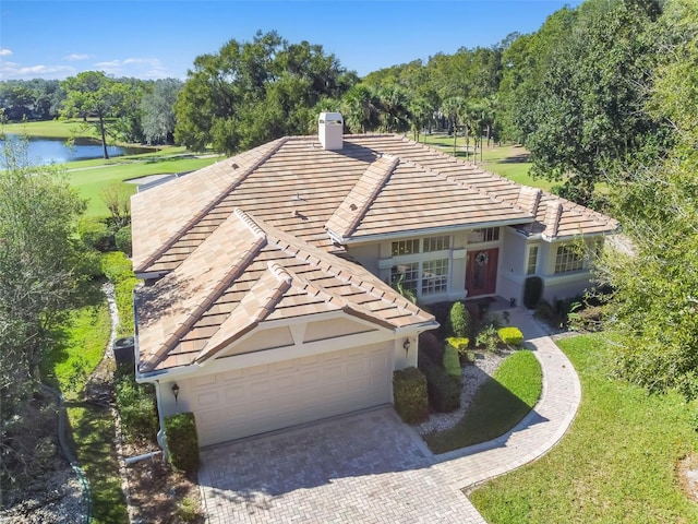 view of front of property featuring decorative driveway, a chimney, a water view, a garage, and a tiled roof