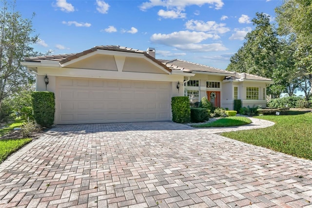 single story home featuring an attached garage, stucco siding, a tile roof, a chimney, and decorative driveway