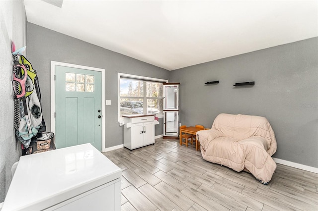 foyer featuring lofted ceiling, light wood-style floors, and baseboards