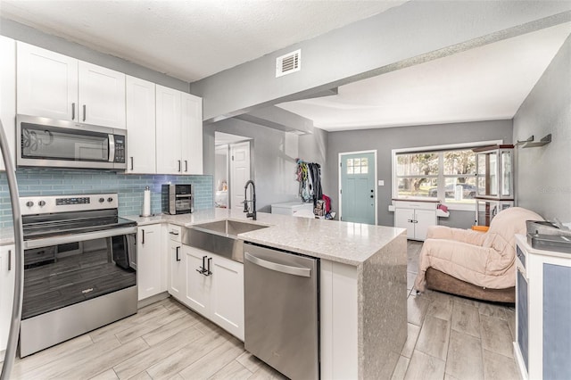 kitchen featuring stainless steel appliances, visible vents, open floor plan, a sink, and a peninsula