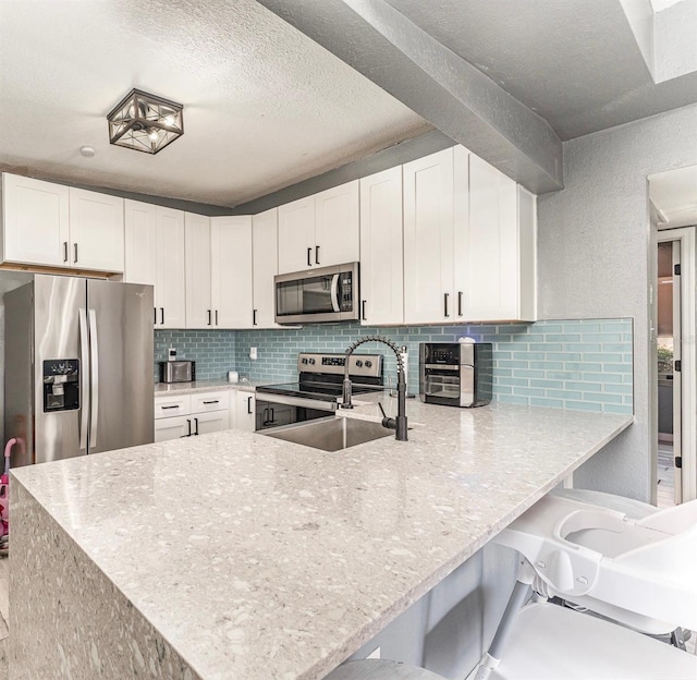 kitchen featuring appliances with stainless steel finishes, a sink, a peninsula, and tasteful backsplash